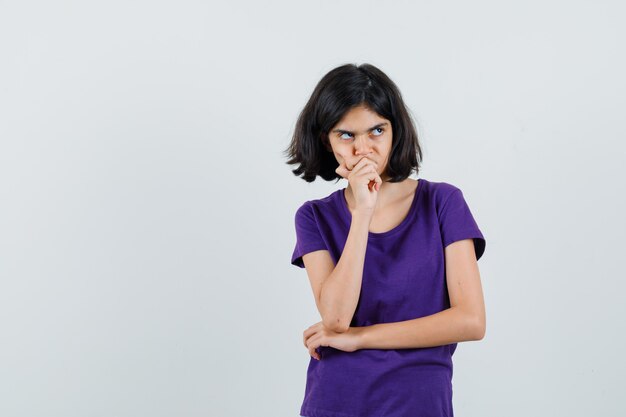 Little girl holding hand on chin in t-shirt and looking pensive ,