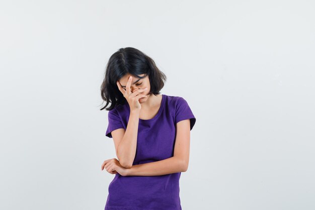 Little girl holding hand on face in t-shirt and looking fatigued. front view.