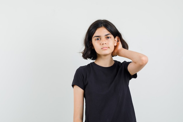 Little girl holding hand in hair in black t-shirt and looking serious , front view.