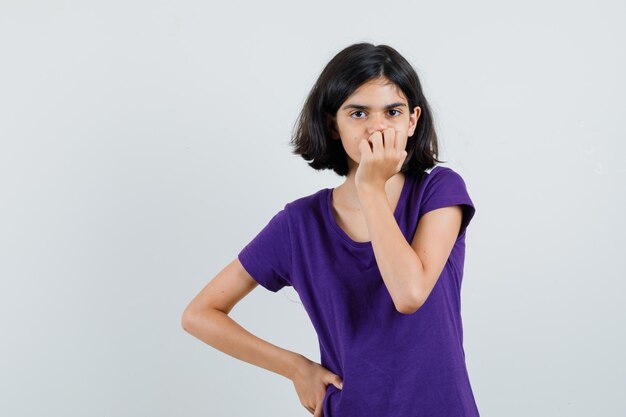 Little girl holding hand on mouth in t-shirt and looking sad.