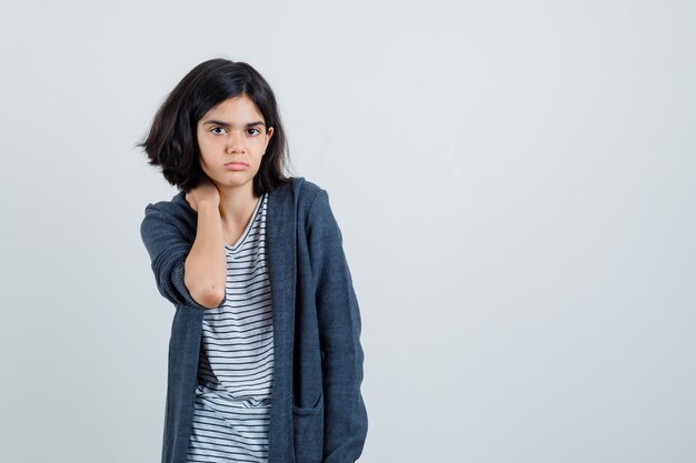 Little girl holding hand on neck in t-shirt, jacket and looking sad ,