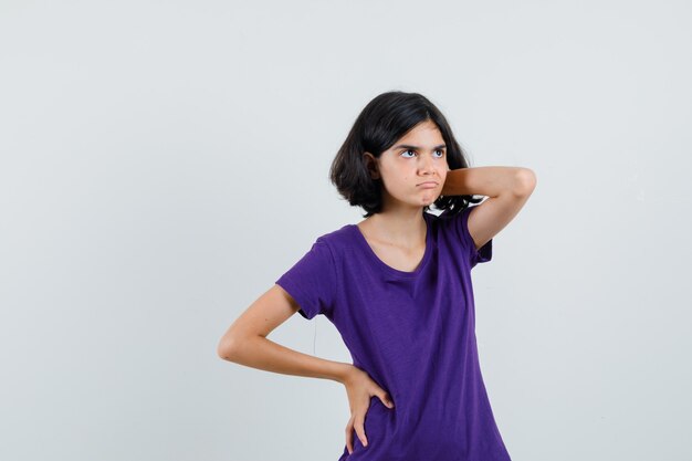 Little girl holding hand on neck in t-shirt and looking hesitant ,