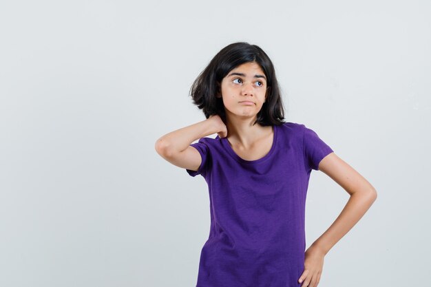 Little girl holding hand on neck in t-shirt and looking indecisive.