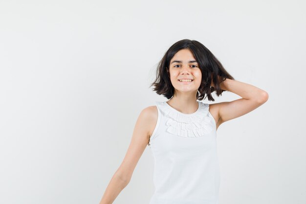 Little girl holding hand on neck in white blouse and looking pretty , front view.