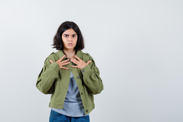 Free photo little girl holding hands on chest in coat, t-shirt, jeans and looking hesitant. front view.