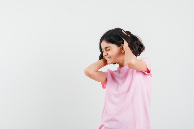 Free photo little girl holding hands in hair in pink t-shirt and looking blissful. front view.