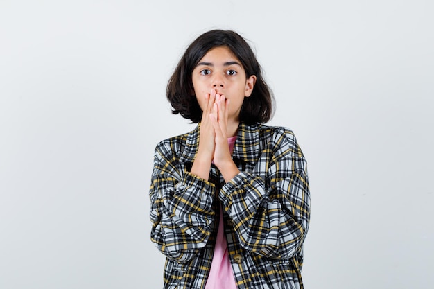 Little girl holding hands on mouth in shirt,jacket and looking horrified. front view.