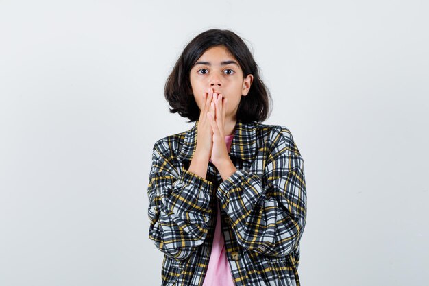 Little girl holding hands on mouth in shirt,jacket and looking horrified. front view.