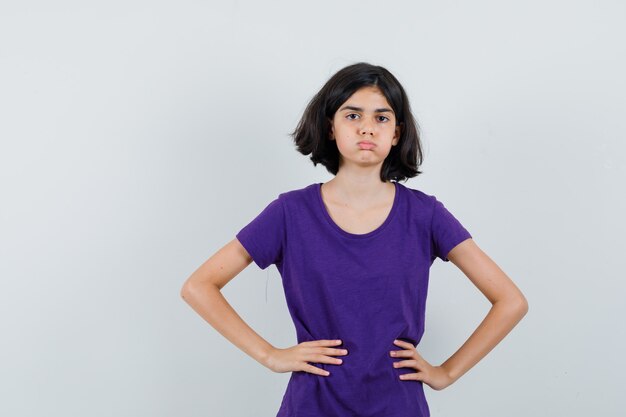 Little girl holding hands on waist in t-shirt and looking exhausted.