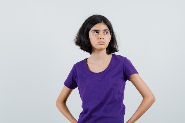 Little girl holding hands on waist in t-shirt and looking sad.