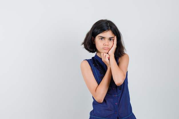 Little girl holding palm on cheek in blue blouse and looking sad. front view.