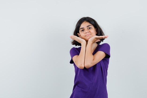 Little girl holding palms under chin in t-shirt and looking cute ,