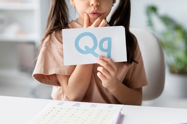 Little girl holding a paper with a letter on it in speech therapy