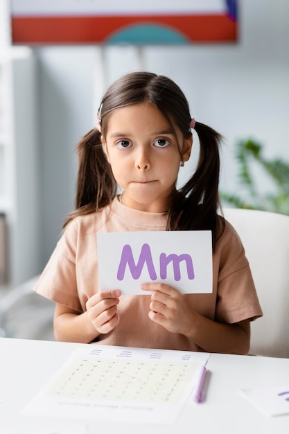 Foto gratuita bambina che tiene una carta con una lettera sopra nella logopedia