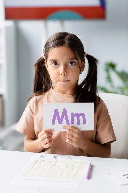 Маленькая девочка держит бумагу с письмом на ней в логопедии