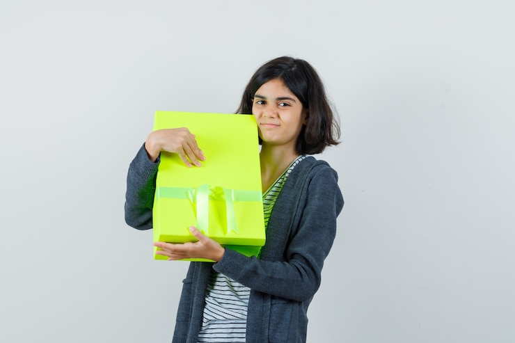 मुफ़्त फोटो little girl holding present box in t-shirt, jacket and looking merry.