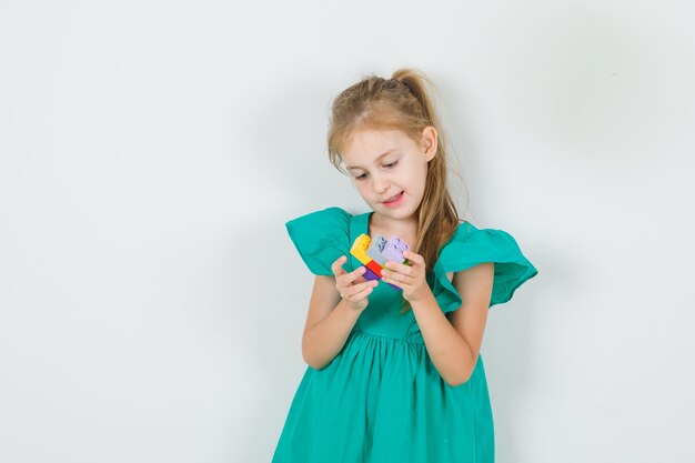 Little girl holding stack of toy blocks in green dress front view.