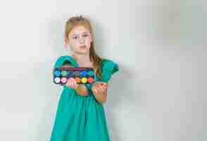 Free photo little girl holding watercolor paints with brush in green dress