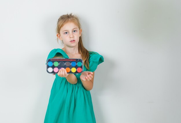 Little girl holding watercolor paints with brush in green dress