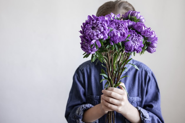 A little girl holds a bouquet of blue chrysanthemums in her hands, copy space.