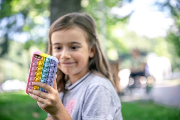 Free photo a little girl holds in her hand a phone in a case with pimples pop it, a trendy anti stress toy.