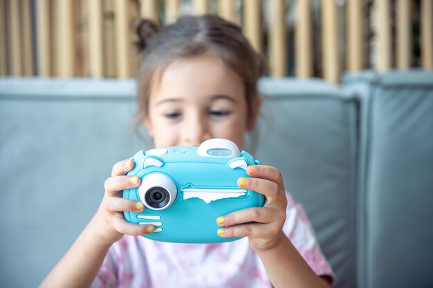 A little girl holds in her hands a blue toy digital camera for children for instant photo printing.