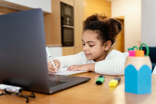 Little girl at home studying during online school with laptop