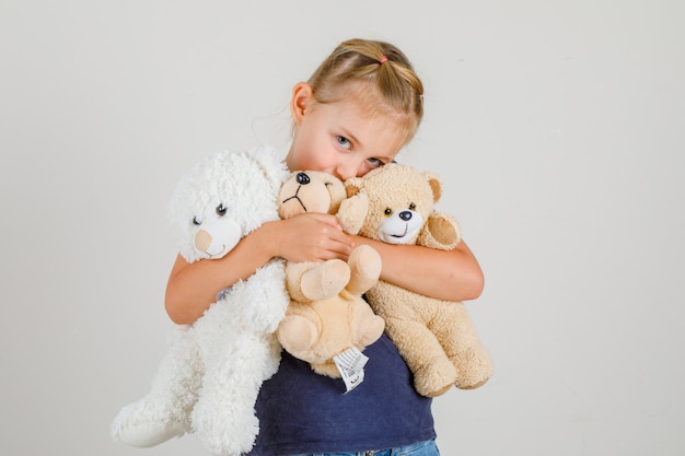 Little girl hugging teddy bears and smiling in t-shirt and denim skirt , front view.