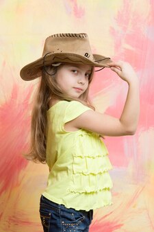 Маленькая девочка в костюме ковбоя или скотницы с поднятой рукой к шляпе на красочном фоне