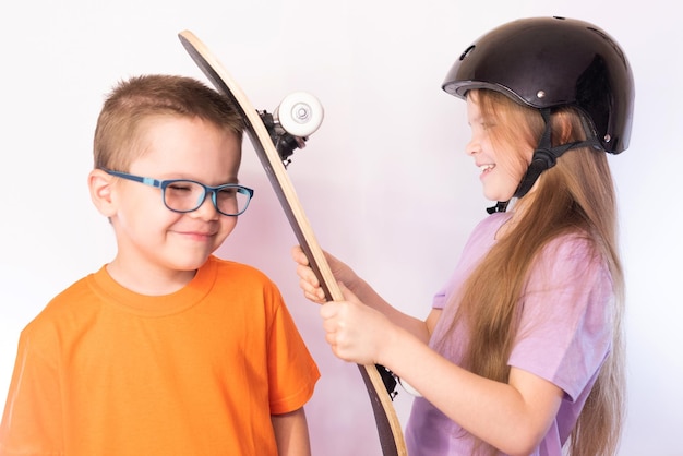 保護ヘルメットをかぶった少女がスケートボードで笑っている少年の頭を打つ