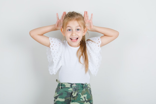 Бесплатное фото Маленькая девочка в белой футболке, юбка показывает руками уши и выглядит смешно