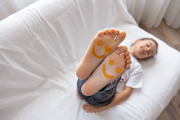 A little girl is lying on a sofa with her feet painted with paints.