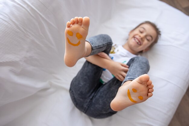 A little girl is lying on a sofa with her feet painted with paints.