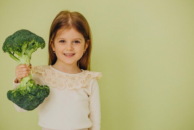 Маленькая девочка изолирована, держа зеленую сырую брокколи