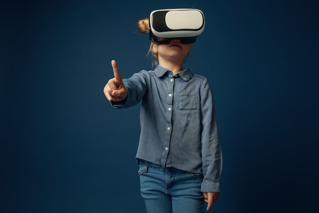 Little girl in jeans and shirt with virtual reality headset glasses isolated