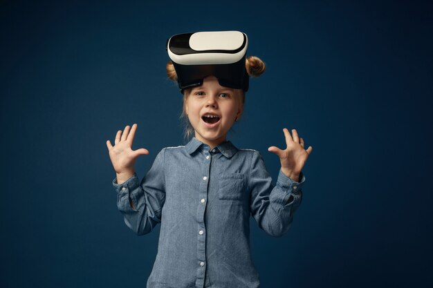 Little girl in jeans and shirt with virtual reality headset glasses isolated