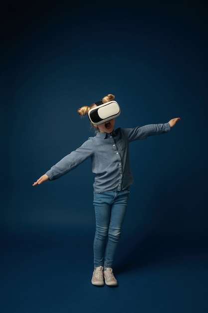 Маленькая девочка в джинсах и рубашке с очками гарнитуры виртуальной реальности изолированы