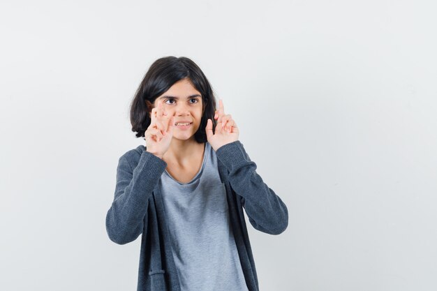 Little girl keeping fingers crossed in t-shirt, jacket and looking dreamy