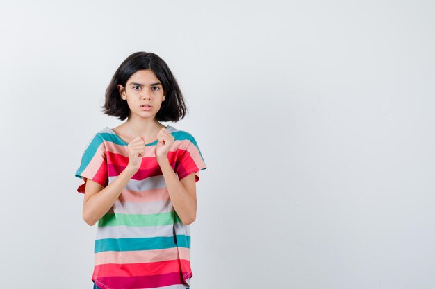 Little girl keeping fists clenched in t-shirt and looking frustrated. front view.