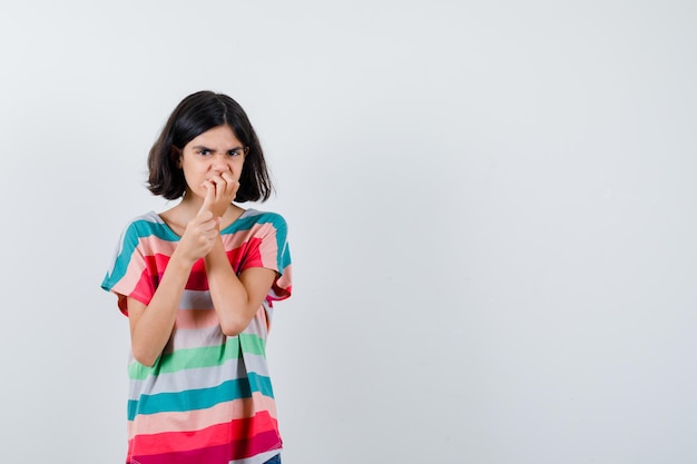 Little girl keeping hand on mouth in t-shirt and looking angry. front view.