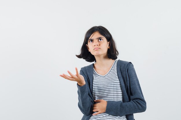 Little girl keeping hand in puzzled gesture in t-shirt, jacket and looking pensive.