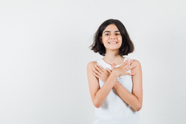 Little girl keeping hands on chest in white blouse and looking nice. front view.