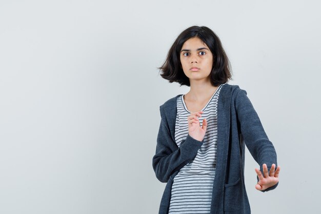 Little girl keeping hands to defend herself in t-shirt, jacket and looking scared ,