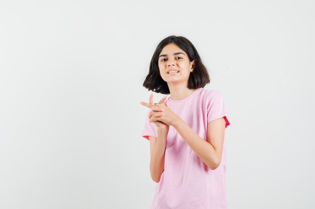 Маленькая девочка держит руки и пальцы, сложенные в розовую футболку, вид спереди.
