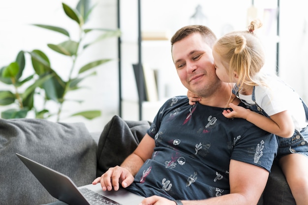 Little girl kissing to her father while working on laptop