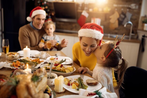 クリスマスの日の家族の昼食時に母親にキスをする少女