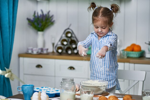 Little girl kneads dough in the kitchen at home. She cooks cookies with love