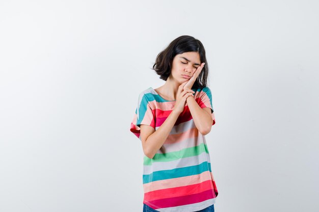 Little girl leaning cheek on palm in t-shirt and looking sleepy. front view.