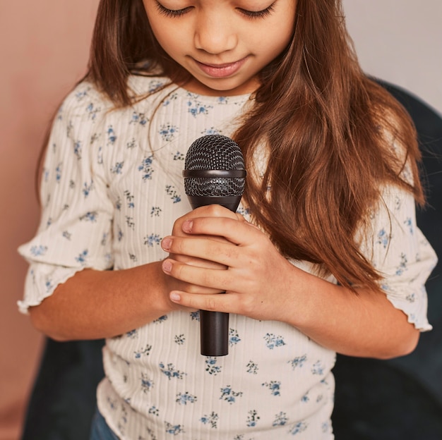 Маленькая девочка учится петь дома с микрофоном