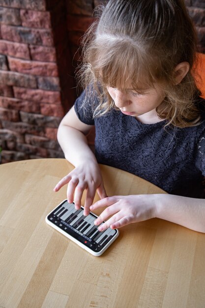 小さな女の子は、携帯電話のピアノの助けを借りて、遊び心のある方法で音符を学びます